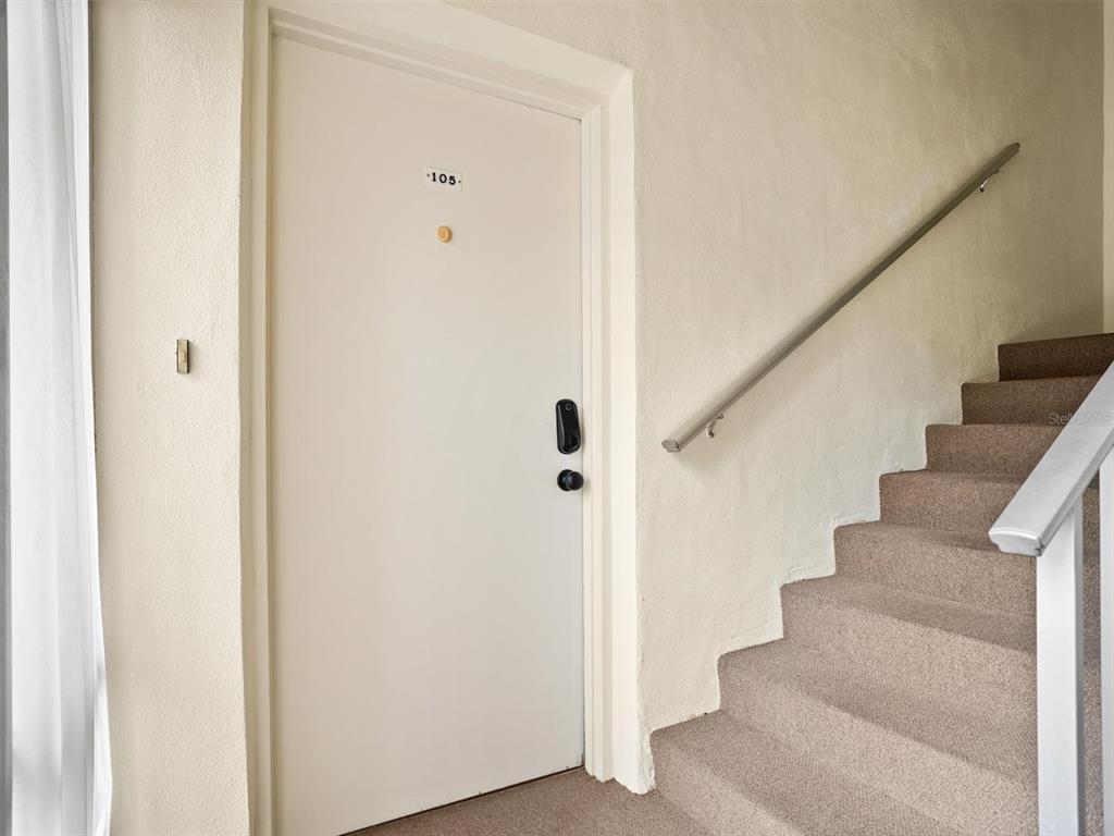 A white apartment door labeled 105 sits next to a carpeted staircase with a handrail — 8303 BARDMOOR BOULEVARD UNIT 105, SEMINOLE, FL