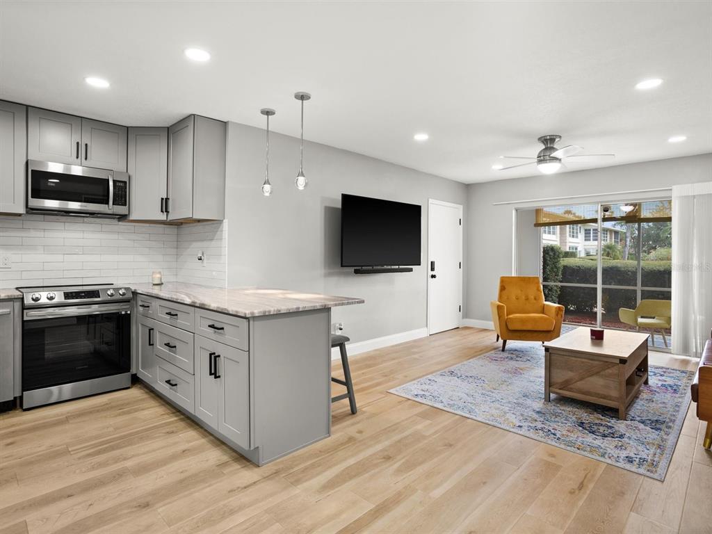 An open-concept kitchen and living area features gray cabinets, light wood flooring, and a patio — 8303 BARDMOOR BOULEVARD UNIT 105, SEMINOLE, FL