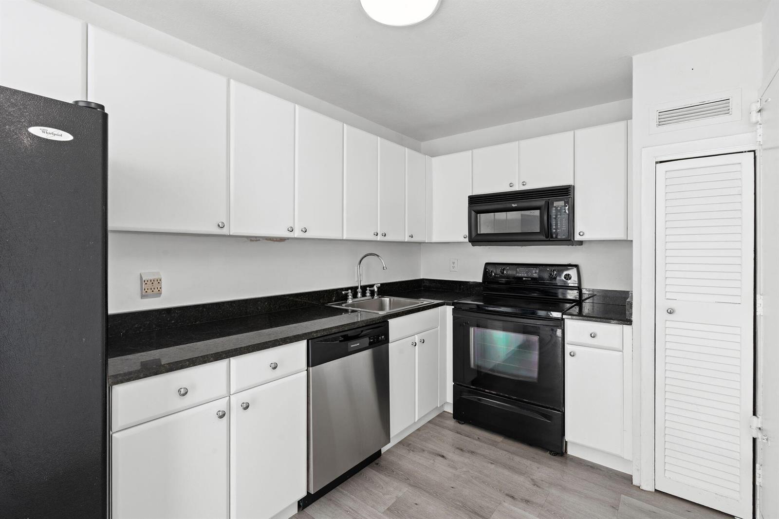 A kitchen with white cabinets, black countertops, stainless steel dishwasher, and black appliances — 1900 S Ocean Boulevard # 10j, Pompano Beach FL 33062, POMPANO BEACH, FL