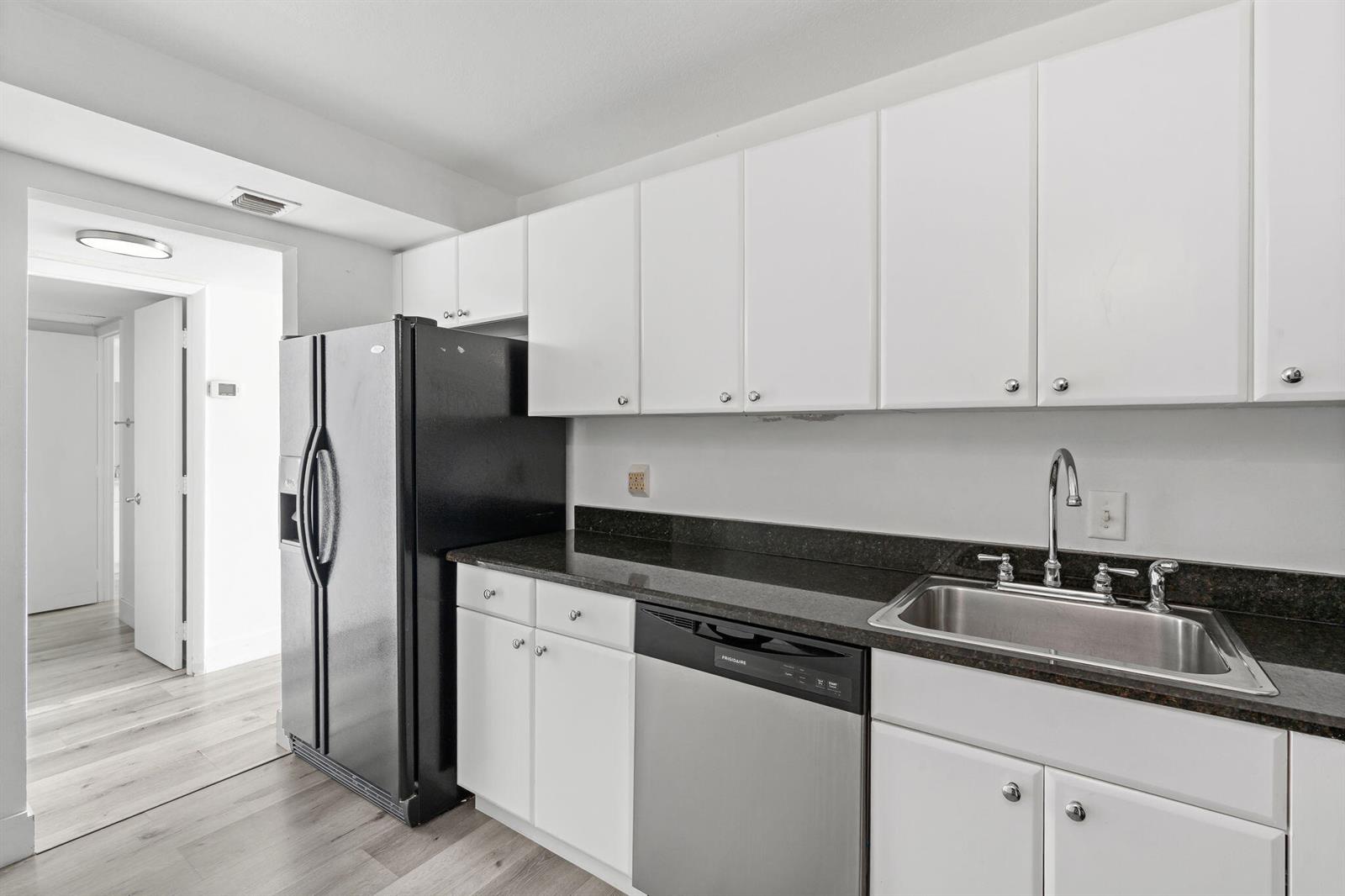 A kitchen features white cabinets, a black refrigerator, a stainless steel dishwasher, and dark countertops — 1900 S Ocean Boulevard # 10j, Pompano Beach FL 33062, POMPANO BEACH, FL