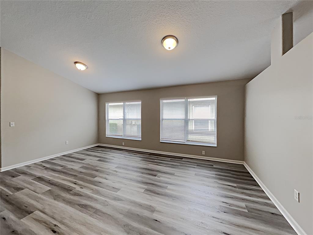 An empty room features light-colored walls, two windows with blinds, and gray wood-look flooring — 3053 EGRETS LANDING DRIVE, LAKE MARY, FL