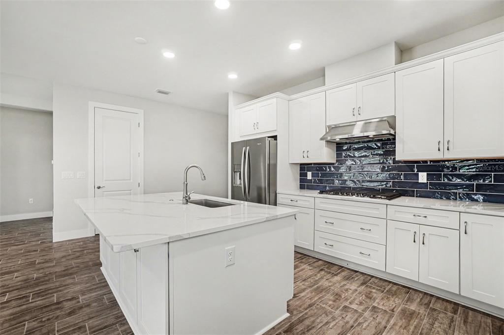 A modern kitchen features white cabinets, a marble-topped island, and a dark blue tiled backsplash — 44353 PANTHER DRIVE, PUNTA GORDA, FL