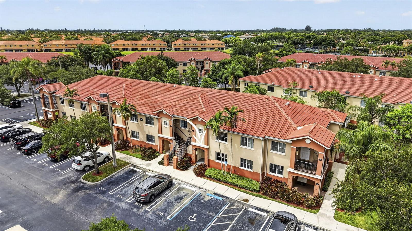 An aerial view of a multi-story apartment building with a red tile roof and parking — 3501 Briar Bay Boulevard # 105, West Palm Beach FL 33411, WEST PALM BEACH, FL