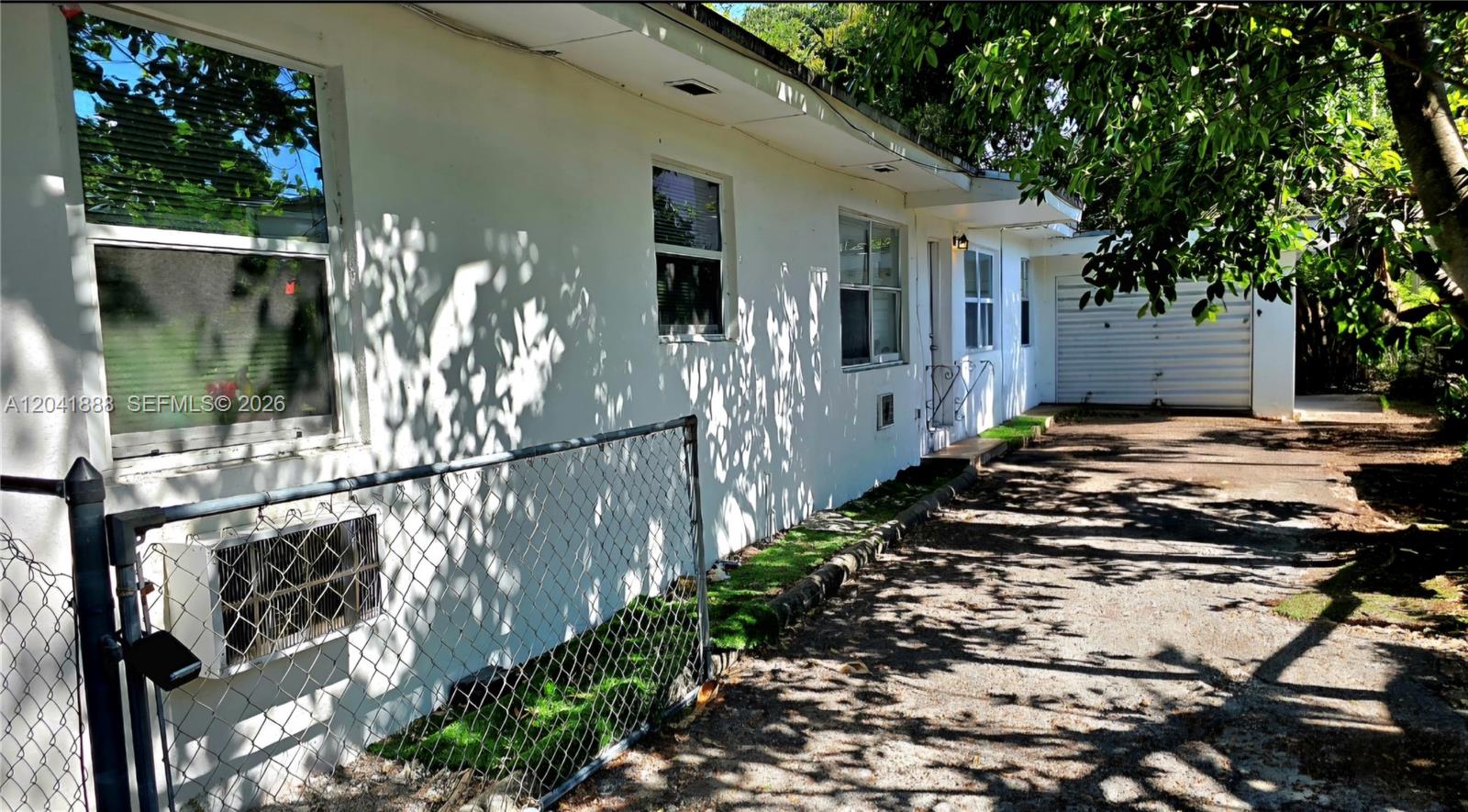 The exterior of a white house features a chain-link fence, windows, and a driveway — 241 NW 32nd St, Miami FL 33127, MIAMI, FL