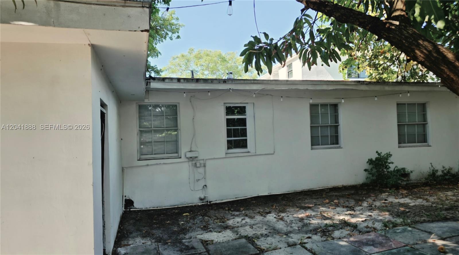 The exterior of a white house features four windows and a paved patio area — 241 NW 32nd St, Miami FL 33127, MIAMI, FL