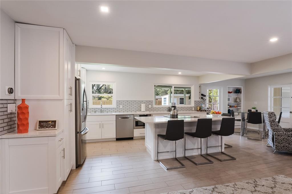 A modern kitchen features white cabinets, a central island with bar seating, and light flooring — 2266 CLEMATIS STREET, SARASOTA, FL
