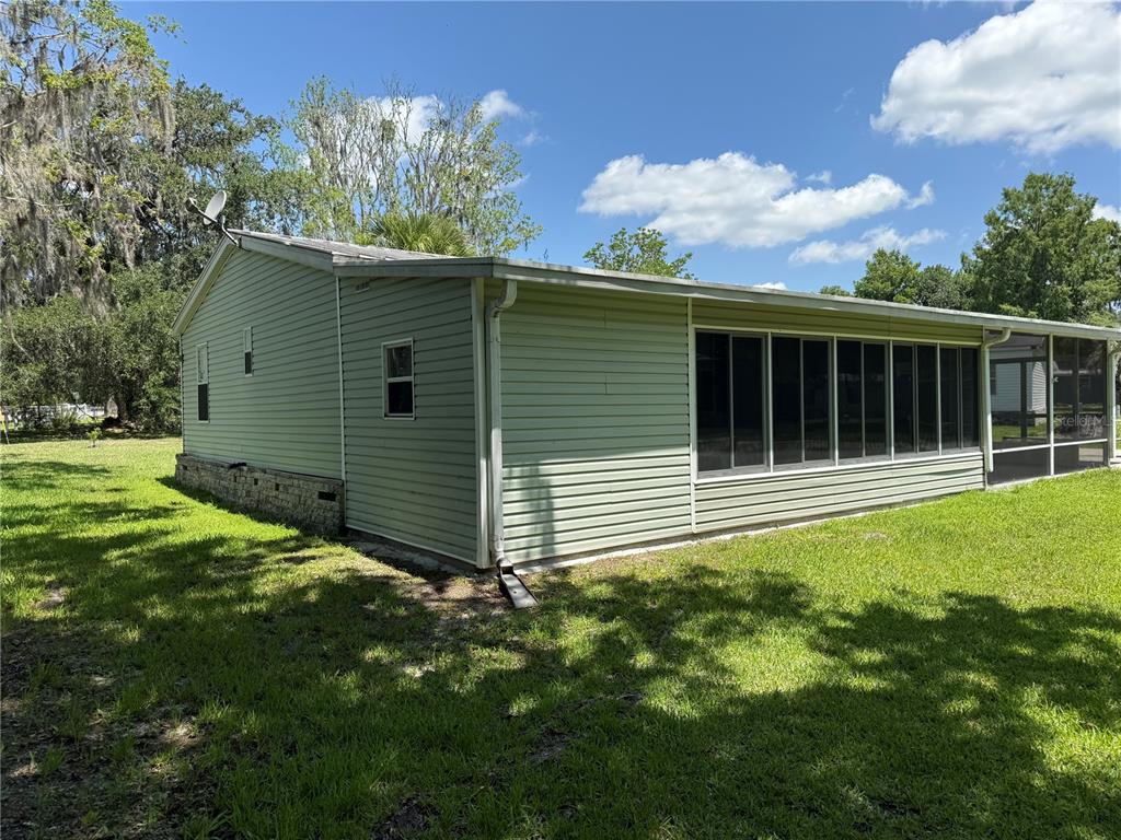 The exterior of a light green house features a screened-in porch and a brick foundation — 26 CANAL WAY, LAKE PANASOFFKEE, FL