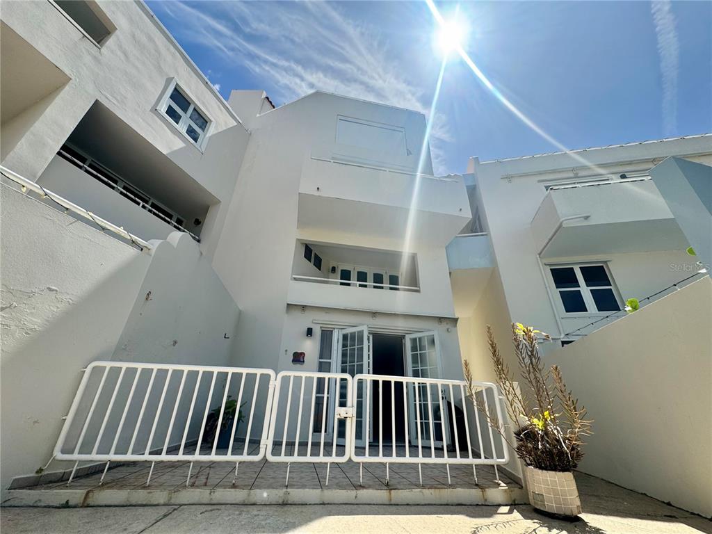 A low-angle exterior view of a white multi-story building with a fenced patio area — 125 HARBOUR DRIVE UNIT 8, HUMACAO, PR