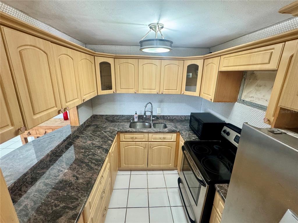 A kitchen features light wood cabinets, dark granite countertops, white tile floors, and stainless appliances — 125 HARBOUR DRIVE UNIT 8, HUMACAO, PR