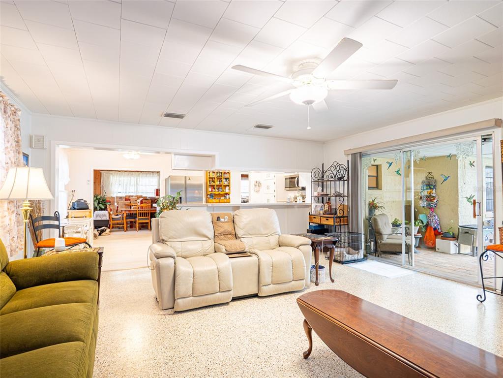 A living room features a beige loveseat, green sofa, ceiling fan, and sliding glass patio doors — 200 S MAIN AVENUE, MINNEOLA, FL