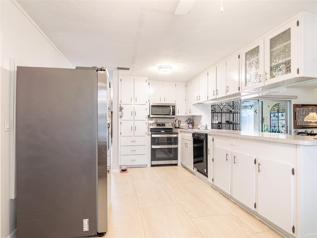 A kitchen features white cabinets, stainless steel appliances, and light-colored tile flooring — 200 S MAIN AVENUE, MINNEOLA, FL
