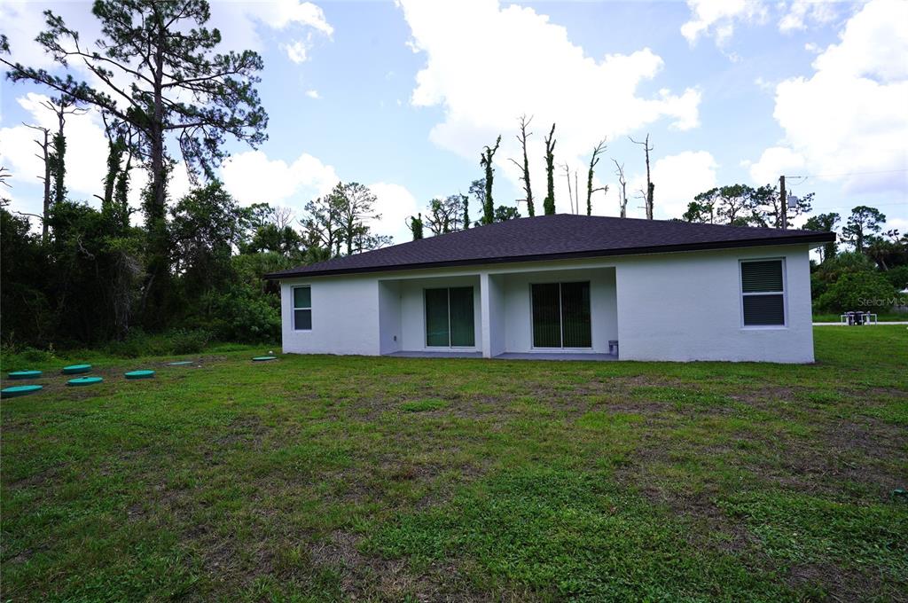 The rear exterior of a white single-story house features a covered patio and sliding doors — 17070 BYRON AVENUE UNIT 17072, PORT CHARLOTTE, FL