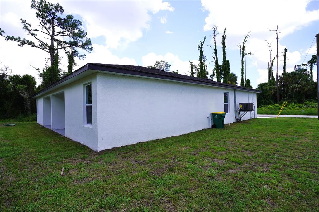 The exterior of a white, single-story house features a dark roof and a green trash bin — 17070 BYRON AVENUE UNIT 17072, PORT CHARLOTTE, FL