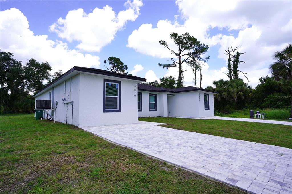 A white single-story house with a paved driveway sits on a grassy lot under a cloudy sky — 17070 BYRON AVENUE UNIT 17072, PORT CHARLOTTE, FL