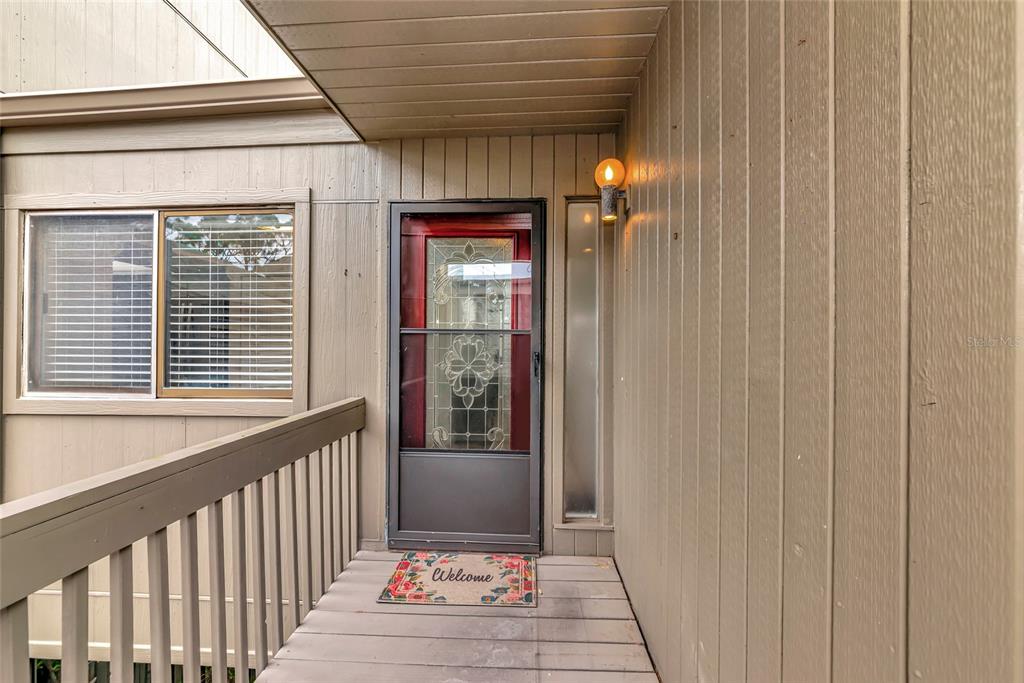 A brown exterior entryway features a wooden deck, a screen door, and a welcome mat — 116 WOODLAND PLACE UNIT 116, OSPREY, FL