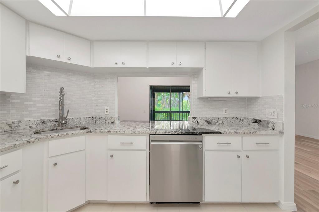 A kitchen with white cabinets, granite countertops, a stainless steel dishwasher, and a pass-through window — 116 WOODLAND PLACE UNIT 116, OSPREY, FL