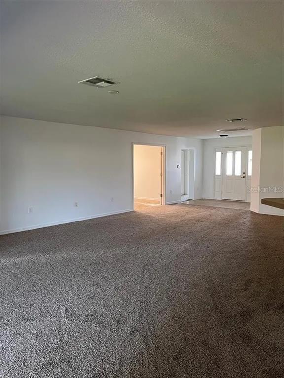 A spacious room with gray carpeting, white walls, and a view of the front door — 8714 SW 83RD LOOP, OCALA, FL