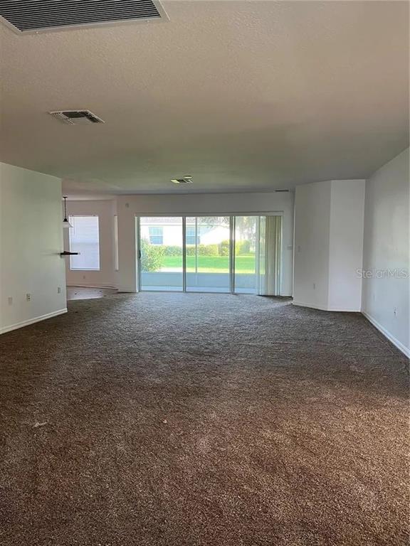 An empty living room with beige carpeting, white walls, and large sliding glass doors — 8714 SW 83RD LOOP, OCALA, FL