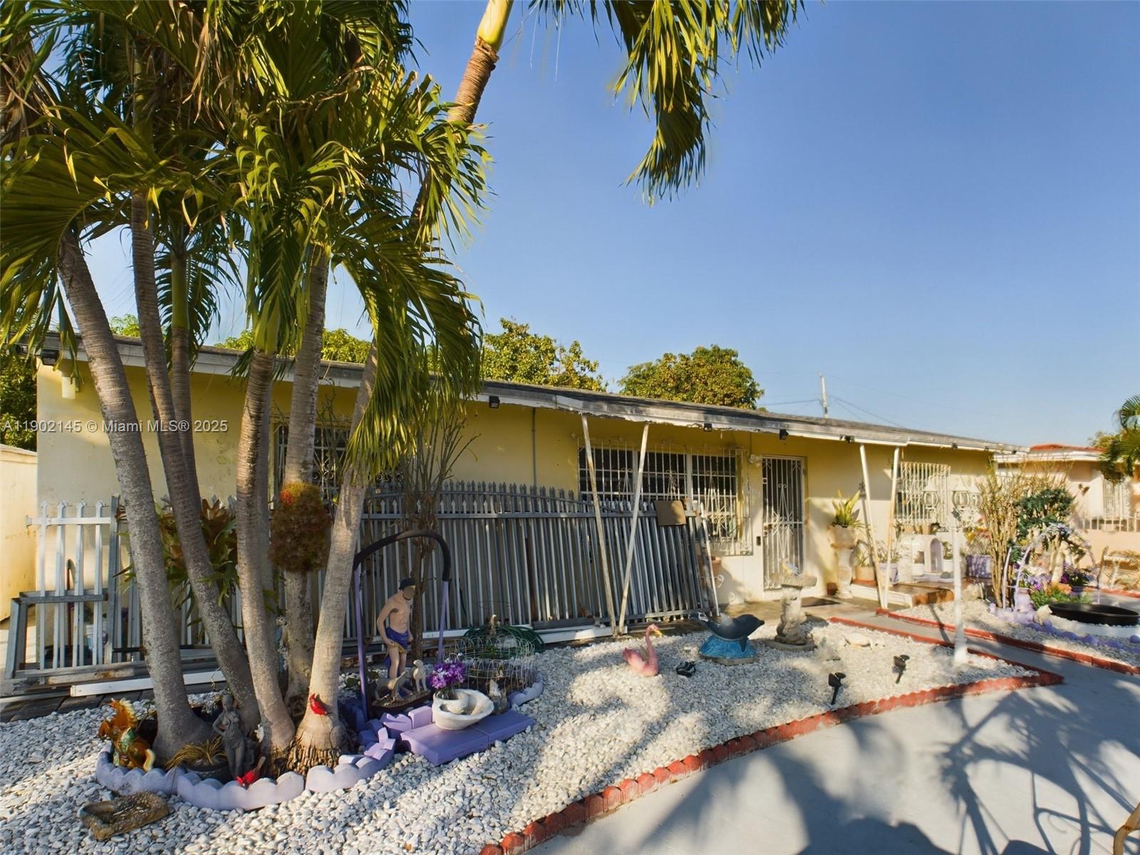 A yellow single-story house features a palm tree, gravel landscaping, and decorative lawn ornaments — 3861 NW 177th St, Miami Gardens FL 33055, MIAMI GARDENS, FL