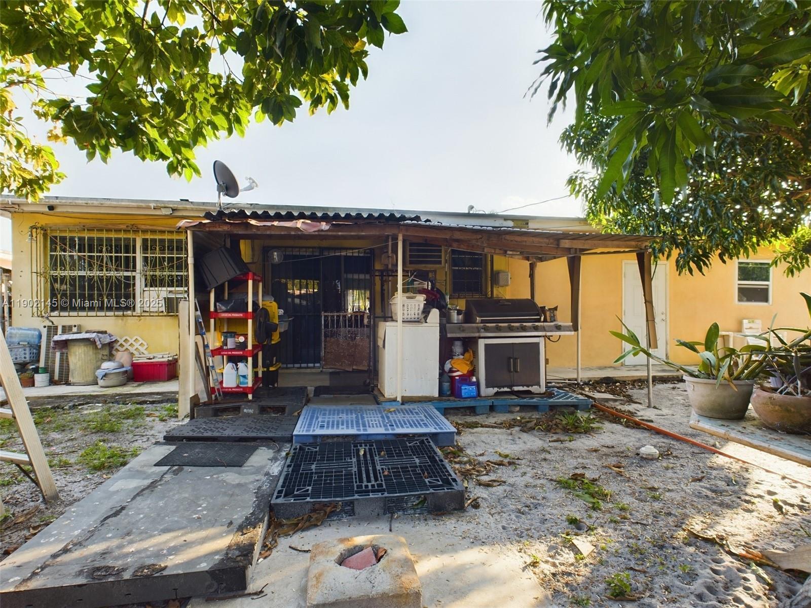 The exterior of a yellow house features a covered patio area with a grill and storage — 3861 NW 177th St, Miami Gardens FL 33055, MIAMI GARDENS, FL