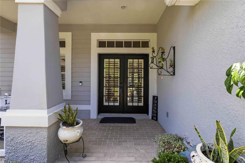 A covered front porch features double glass-paneled doors, brick flooring, and potted plants — 16817 HARRIERRIDGE PLACE, LITHIA, FL