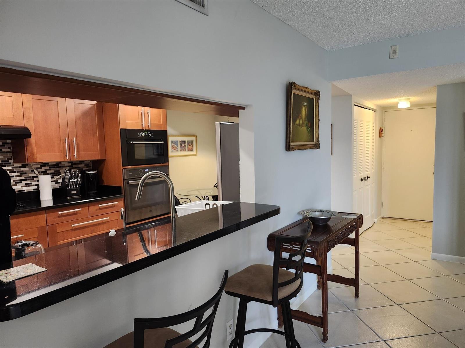 A kitchen with wood cabinets and black countertops overlooks a hallway with tiled floors — 450 Egret Circle, Delray Beach FL 33444, DELRAY BEACH, FL