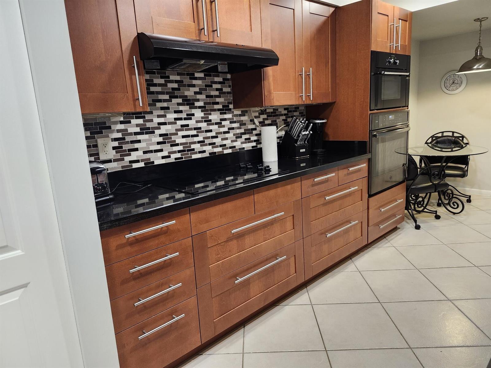 A kitchen features wood cabinets, black countertops, a mosaic tile backsplash, and stainless steel appliances — 450 Egret Circle, Delray Beach FL 33444, DELRAY BEACH, FL