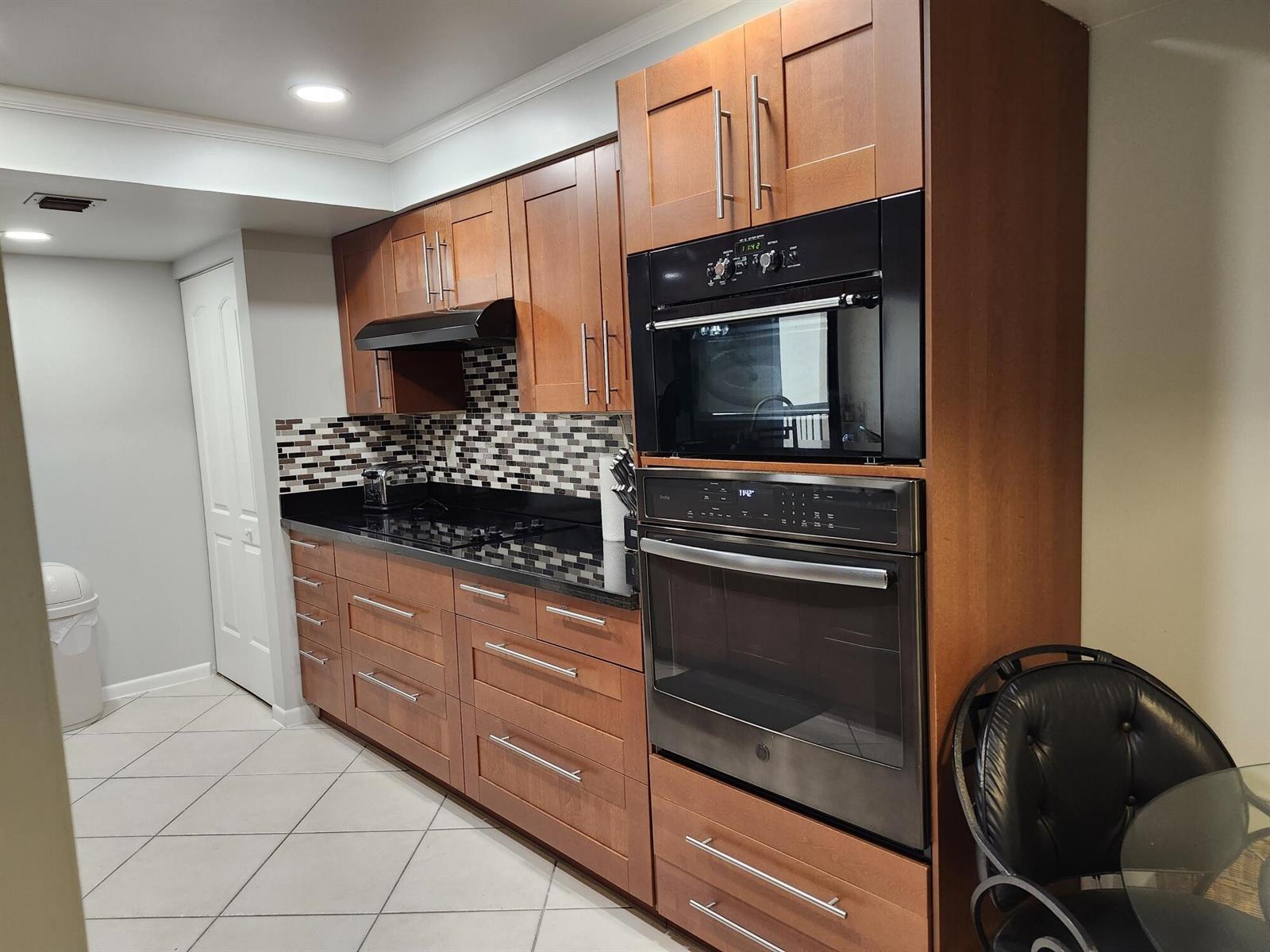 A kitchen features wood cabinets, black appliances, a tiled backsplash, and dark countertops — 450 Egret Circle, Delray Beach FL 33444, DELRAY BEACH, FL