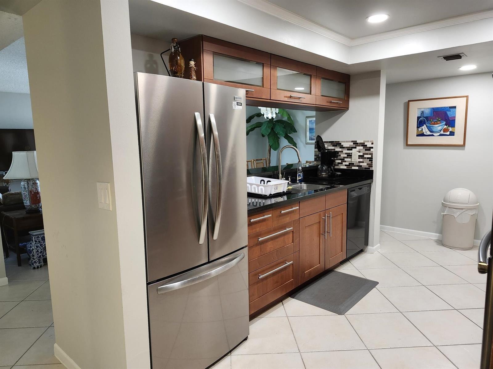 A kitchen features stainless steel appliances, wood cabinets, black countertops, and a tile floor — 450 Egret Circle, Delray Beach FL 33444, DELRAY BEACH, FL