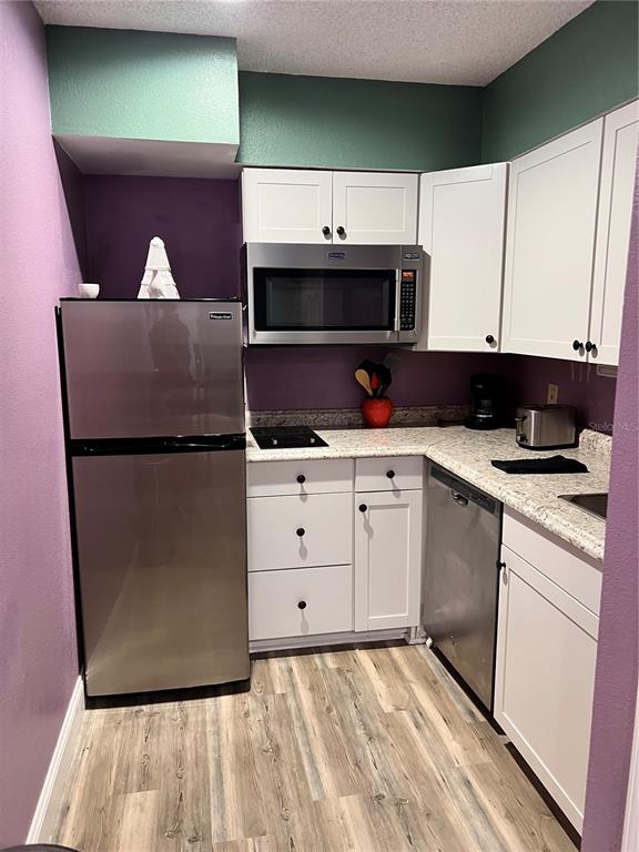A small kitchen features white cabinets, stainless steel appliances, and purple walls — 3100 PARKWAY BOULEVARD UNIT 521, KISSIMMEE, FL