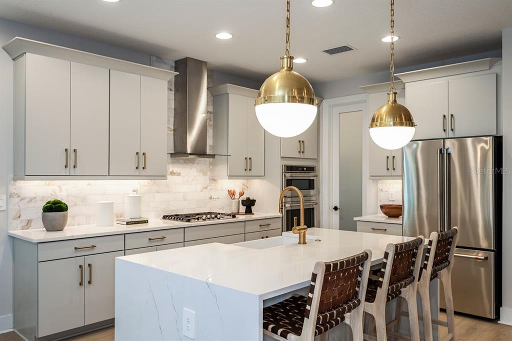 A modern kitchen features light gray cabinets, a white marble island, and two gold pendant lights — 13694 LOREDO WAY, PUNTA GORDA, FL