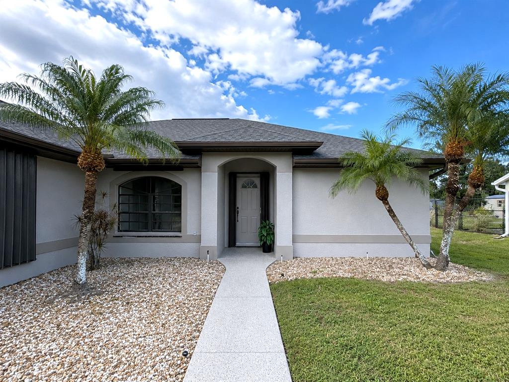 The exterior of a single-story house features a concrete walkway, two palm trees, and gravel landscaping — 23146 AMBASSADOR AVENUE, PORT CHARLOTTE, FL