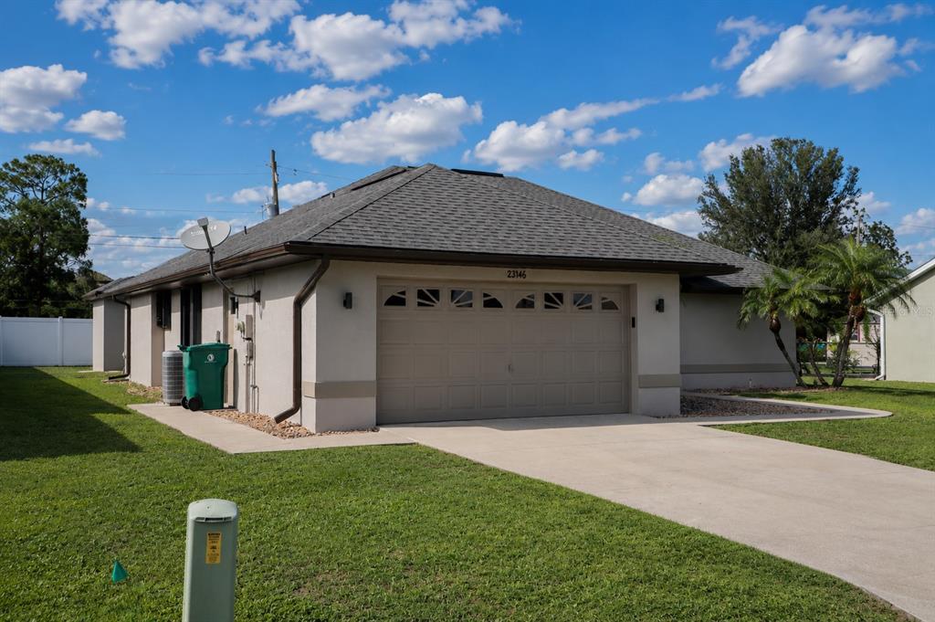 A single-story house exterior features a beige stucco facade, a gray shingled roof, and garage — 23146 AMBASSADOR AVENUE, PORT CHARLOTTE, FL