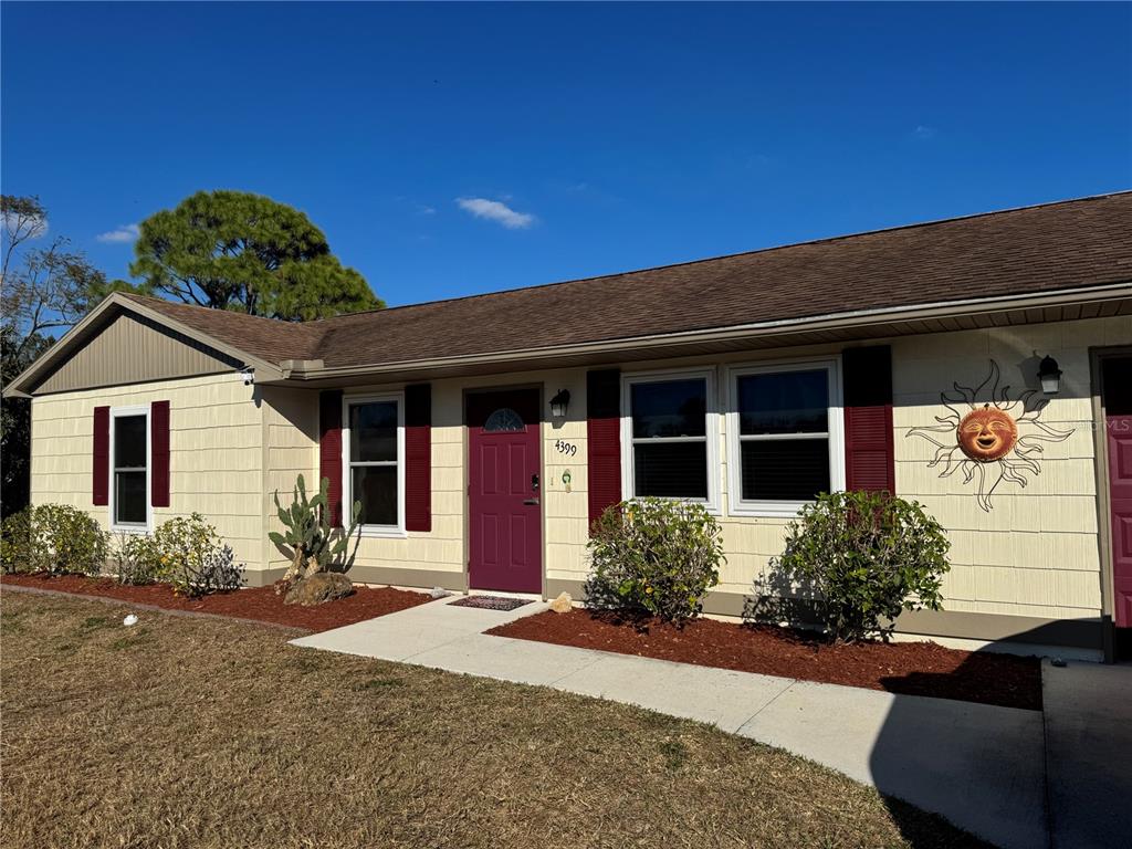 A single-story house with beige shingle siding, a maroon front door, and a sun wall decoration — 4399 MUNDELLA CIRCLE, PORT CHARLOTTE, FL