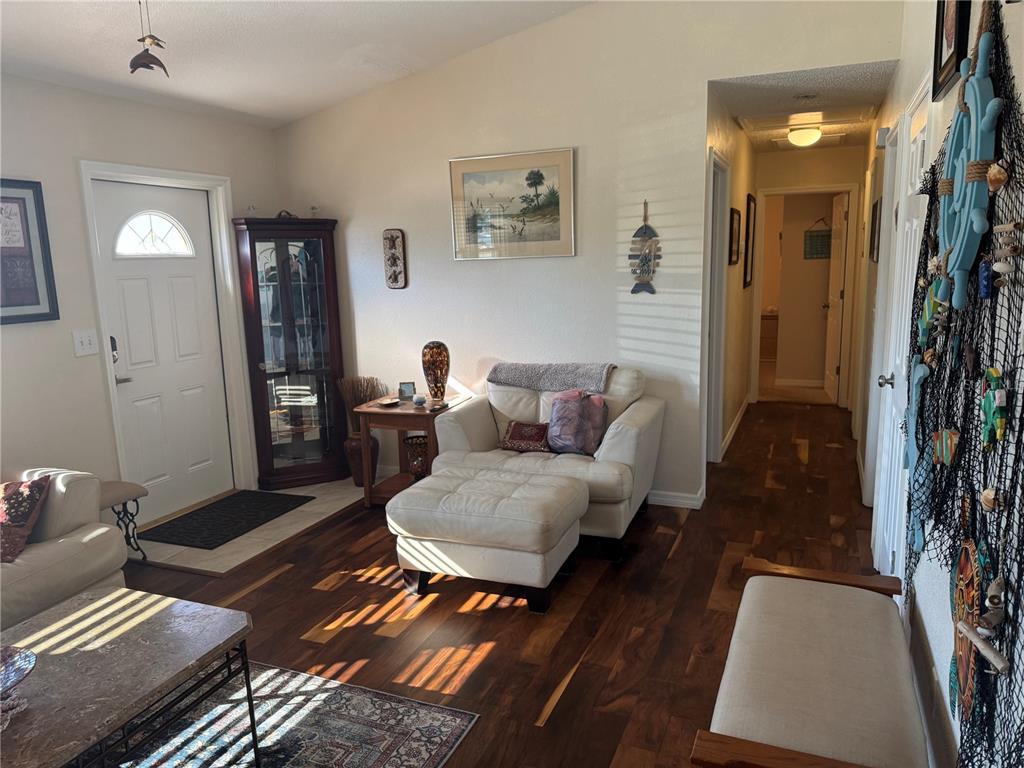 A living room features dark wood flooring, a white armchair with ottoman, and a front door — 4399 MUNDELLA CIRCLE, PORT CHARLOTTE, FL