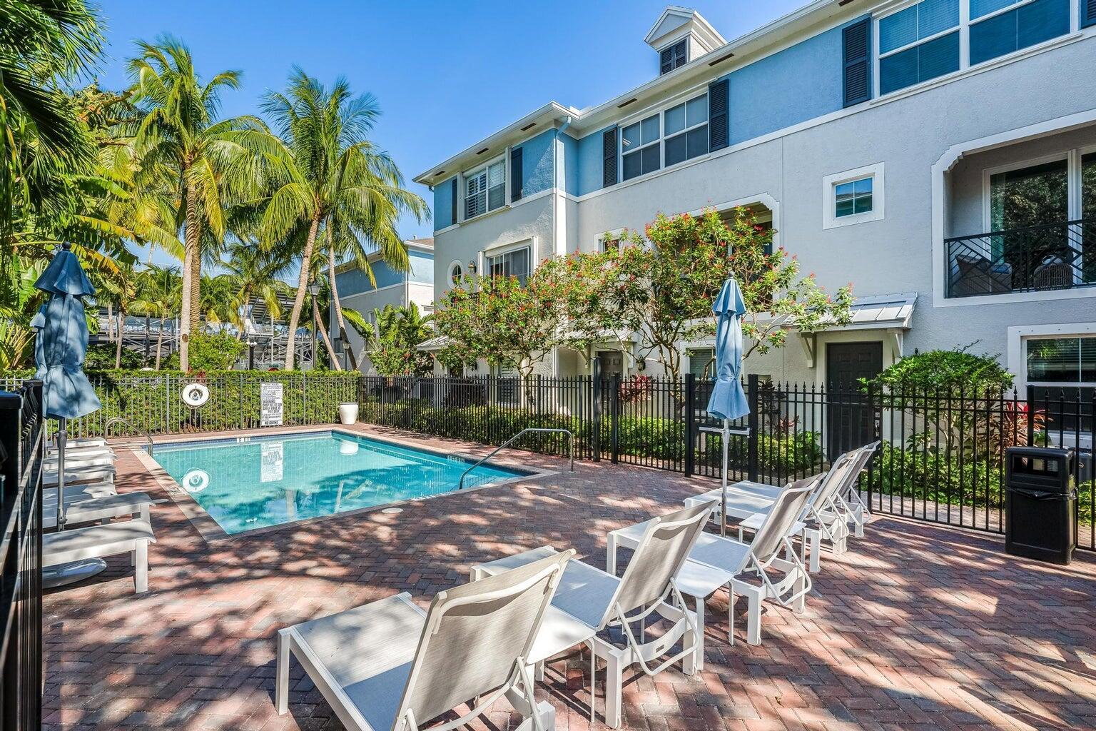 A swimming pool with lounge chairs on a brick patio beside a multi-story building — 75 Atlantic Grove Way, Delray Beach FL 33444, DELRAY BEACH, FL
