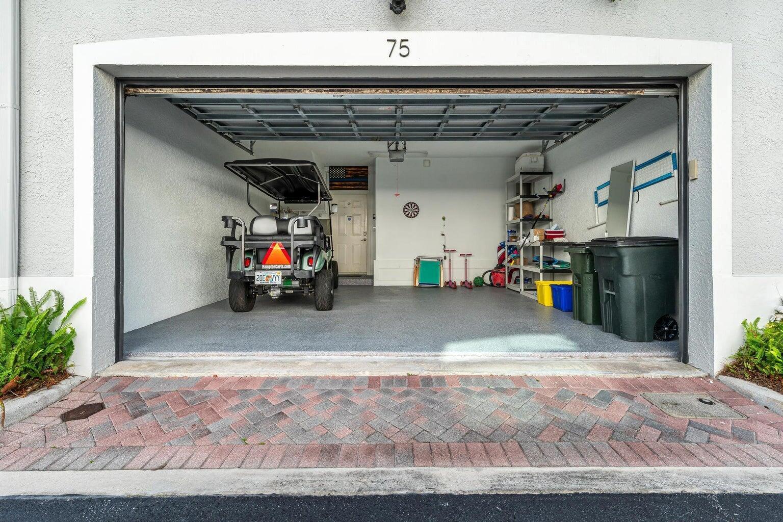 An open garage with a golf cart, storage shelving, and a concrete floor — 75 Atlantic Grove Way, Delray Beach FL 33444, DELRAY BEACH, FL
