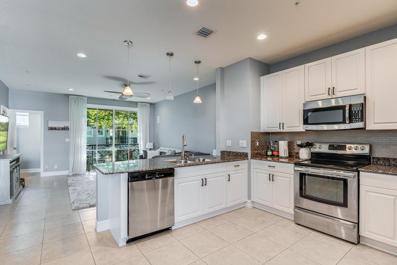 A kitchen with white cabinets, granite countertops, and stainless steel appliances opens to a living area — 75 Atlantic Grove Way, Delray Beach FL 33444, DELRAY BEACH, FL