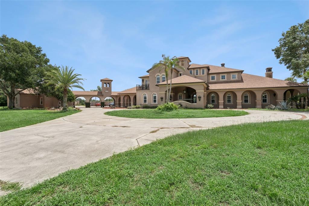 A paved driveway leads to a gated entrance flanked by stone pillars and mature trees — 9400 LAWS RD, CLERMONT, FL