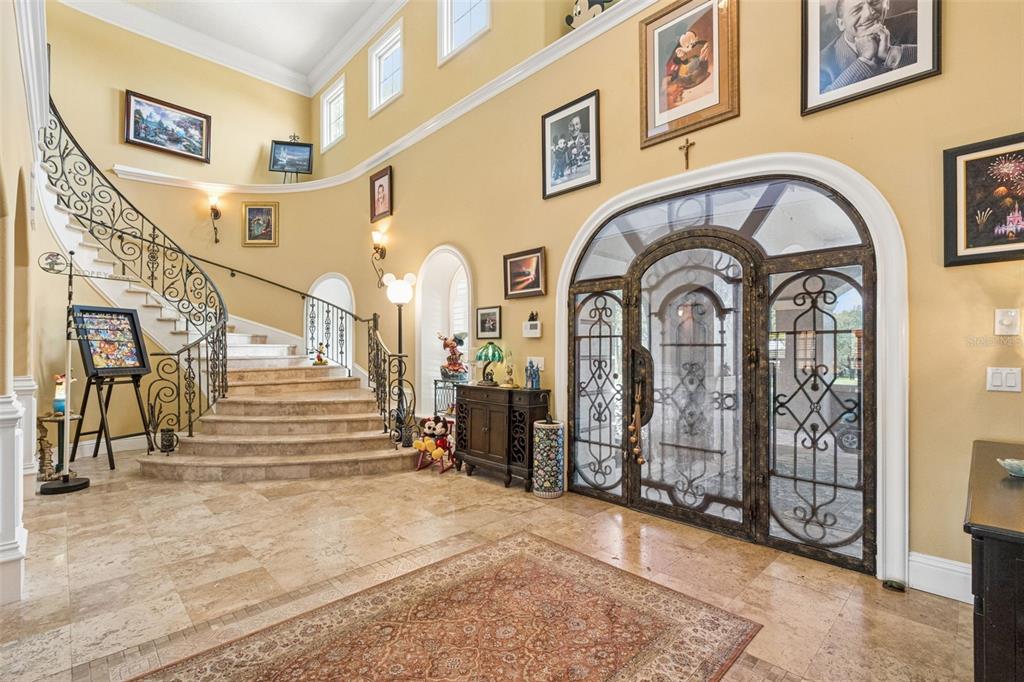 A grand foyer features a curved staircase, stone flooring, and an ornate arched metal door — 9400 LAWS RD, CLERMONT, FL