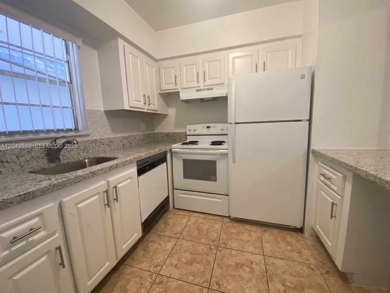 A kitchen features white cabinets, granite countertops, white appliances, and light-colored tile flooring — 6501 Winfield Blvd # 53, Margate FL 33063, MARGATE, FL