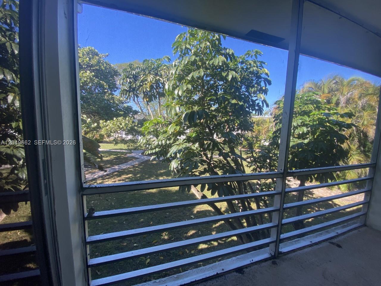 A view of a grassy courtyard with trees seen through a screened-in balcony — 6501 Winfield Blvd # 53, Margate FL 33063, MARGATE, FL