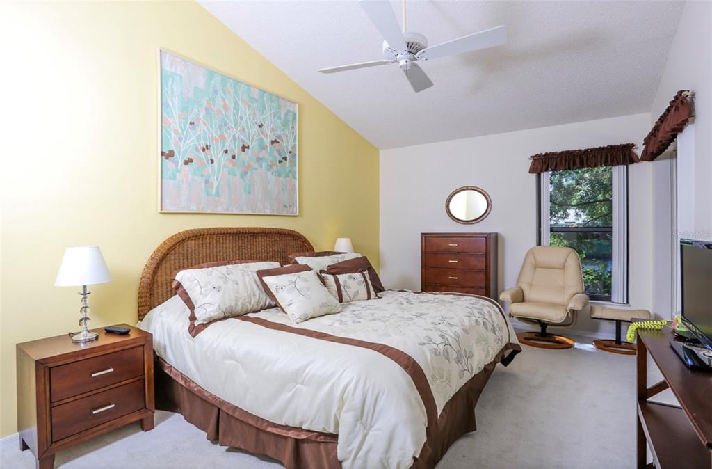 A bedroom with a wicker headboard, yellow accent wall, ceiling fan, and a beige armchair — 226 SOUTHAMPTON LANE UNIT 257, VENICE, FL