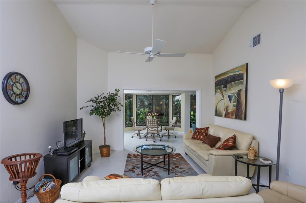 A living room with white walls, a vaulted ceiling, a ceiling fan, and beige sofas — 226 SOUTHAMPTON LANE UNIT 257, VENICE, FL