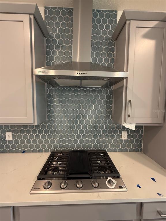 A kitchen features a gas cooktop, stainless steel range hood, and blue hexagonal tile backsplash — 5119 BUTTONSAGE DRIVE, ST CLOUD, FL