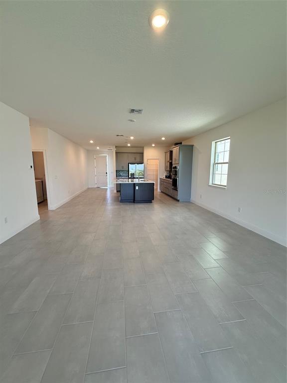 An open-concept kitchen and living area features light gray tile flooring and a central island — 5119 BUTTONSAGE DRIVE, ST CLOUD, FL