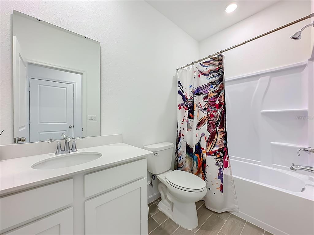 A bathroom features a white vanity, a toilet, and a shower-tub combination with a patterned curtain — 3153 TUPELO LOOP, GREEN COVE SPRINGS, FL