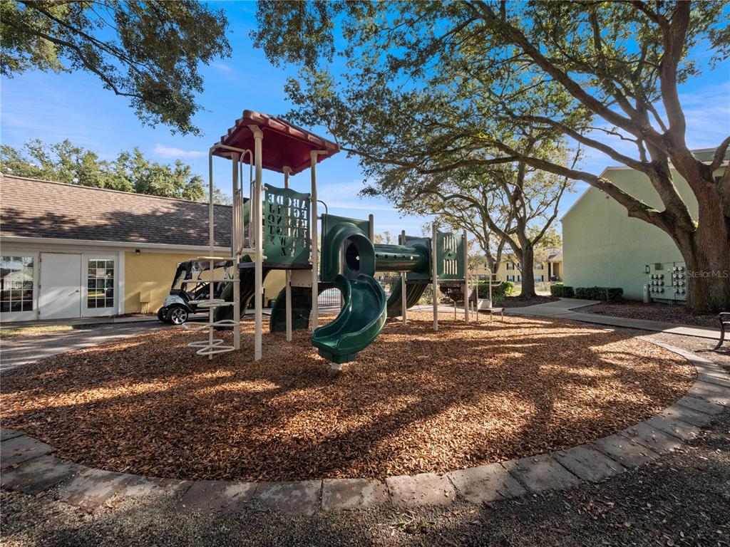 A playground with a green slide and climbing structure sits on wood chips outdoors — 2077 DIXIE BELLE DRIVE UNIT 2077C, ORLANDO, FL