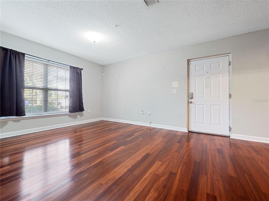 An empty room features dark wood flooring, light gray walls, a window with curtains, and a door — 2077 DIXIE BELLE DRIVE UNIT 2077C, ORLANDO, FL