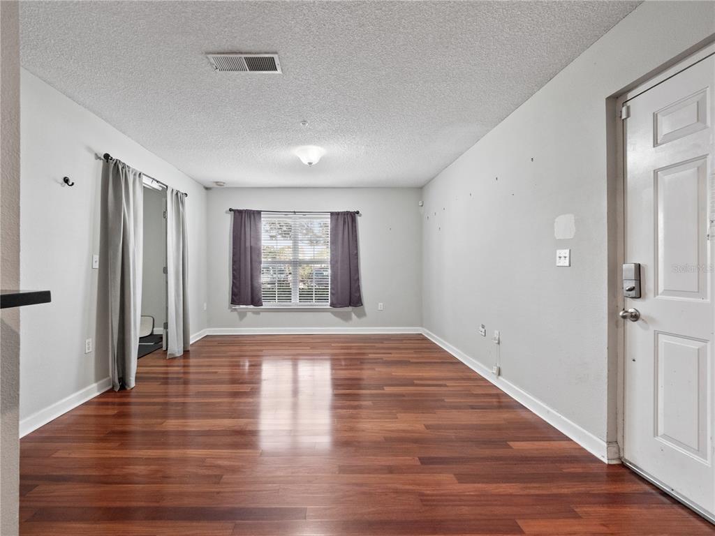 An empty living room features hardwood floors, light gray walls, and a single window — 2077 DIXIE BELLE DRIVE UNIT 2077C, ORLANDO, FL